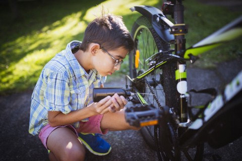 Mixed race boy oiling bicycle chain in backyard