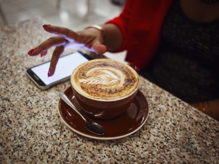 Mixed race woman using cell phone with coffee in cafe