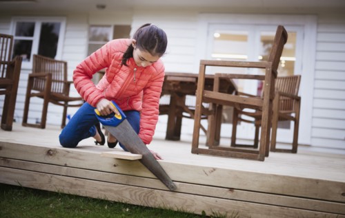 Mixed race girl sawing wood in backyard