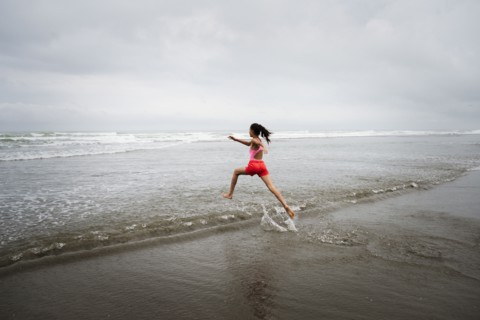 Mixed race girl running into ocean on beach