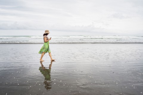 Mixed race woman walking on beach with cell phone
