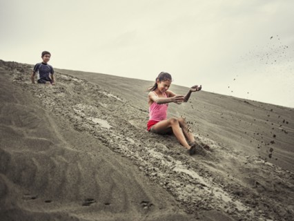 Children sliding on sand dune