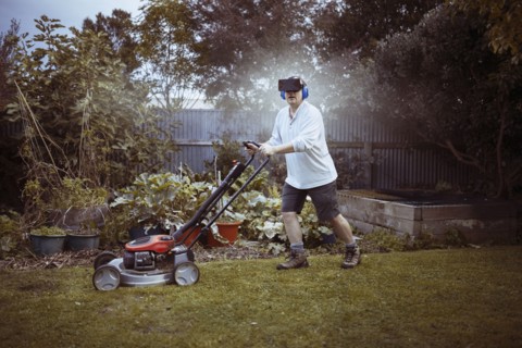 Caucasian man mowing lawn with VR goggles