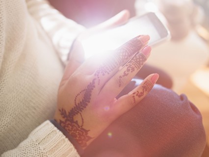 Woman with henna tattoos on hands texting on cell phone