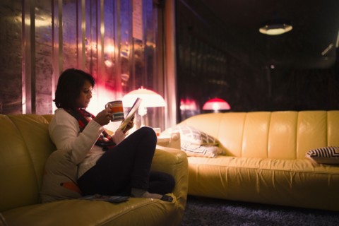 Woman drinking tea and reading magazine on sofa
