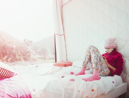 Mixed Race girl sitting on bed texting on cell phone