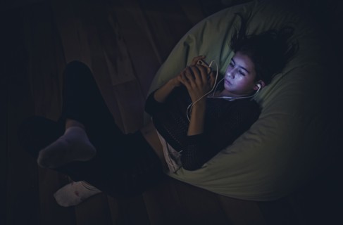 Mixed Race girl using cell phone laying on bean bag in dark