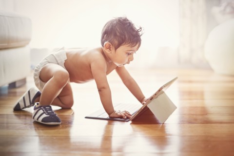 Indian baby boy crawling on floor with digital tablet