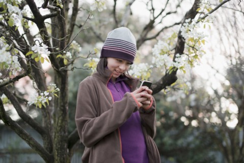 Smiling Mixed Race girl texting on cell phone near tree