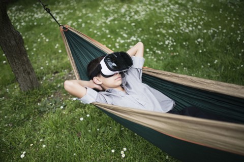 Mixed Race boy laying in hammock wearing virtual reality goggles