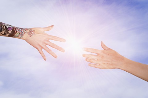 Hands with tattoos and freckles reaching in sky