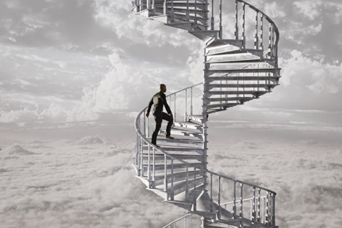 Man climbing spiral staircase in the clouds