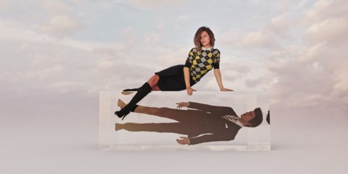 Confident businesswoman sitting on cube with businessman trapped inside