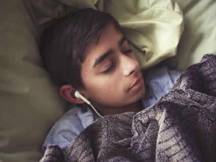 Mixed race boy laying in bed listening to earbuds