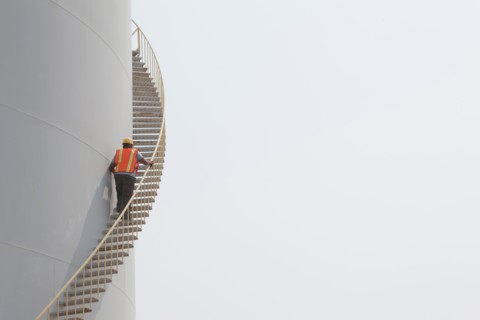 Mixed race worker climbing staircase on storage tank