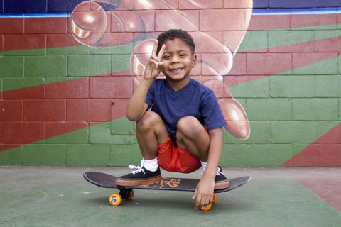 African American boy sitting on skateboard by urban mural