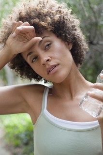 Mixed race woman wiping forehead and drinking water