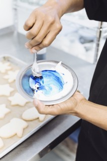 Close up of baker making blue frosting in bakery