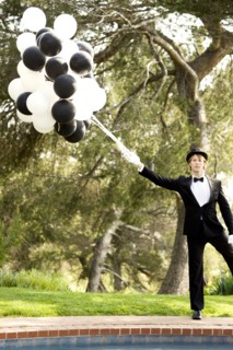 Caucasian man in tuxedo holding bunch of balloons