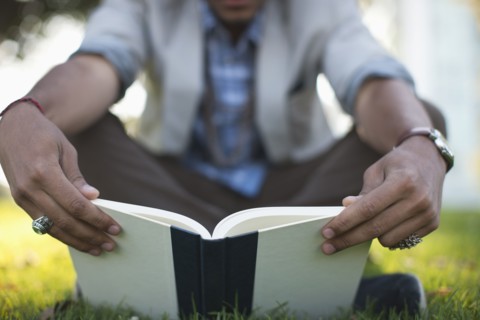 Hispanic man reading book in grass