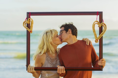 Caucasian couple holding frame with hearts and kissing