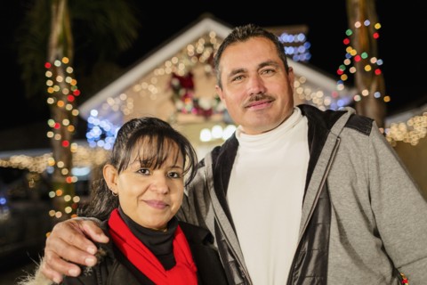 Hispanic couple smiling outside house decorated with string lights