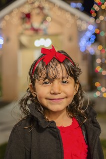 Hispanic girl smiling outside house decorated with string lights