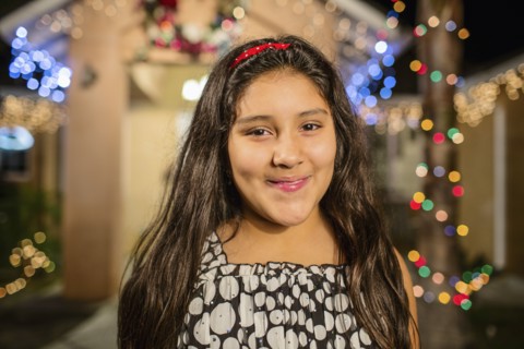 Hispanic girl smiling outside house decorated with string lights
