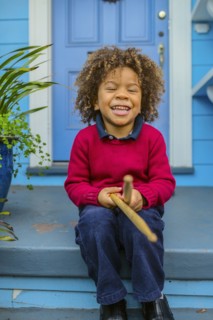 Pacific Islander boy with drumsticks sitting on front stoop