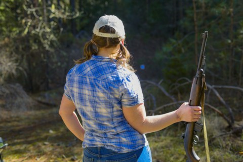 Caucasian woman carrying rifle in forest