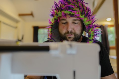 Caucasian man wearing fuzzy hat using sewing machine