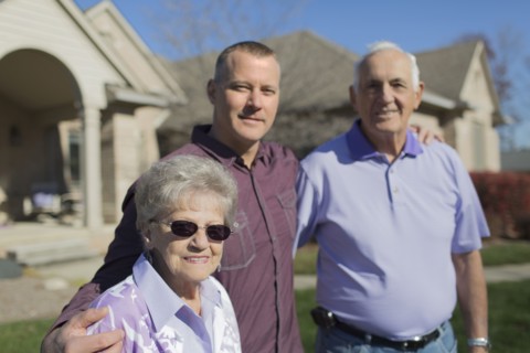 Older Caucasian parents and son smiling in yard