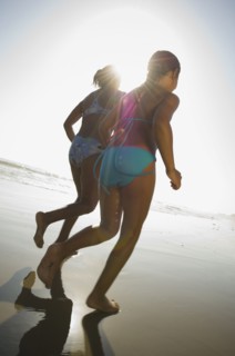 Hispanic mother and daughter running at beach