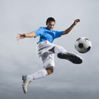 Mixed race teenager in mid-air kicking soccer ball