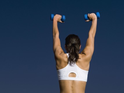 Rear view of mixed race woman holding dumbbells overhead