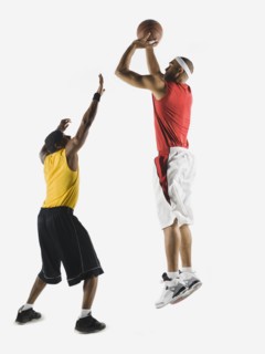 African man shooting basketball over opponent