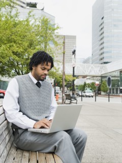 Mixed race businessman using laptop on city bench