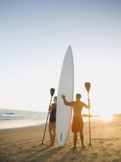 Couple standing on beach with surfboard and paddles