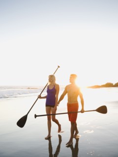 Couple walking on beach carrying paddles