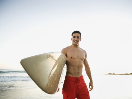 Mixed race man carrying surfboard on beach