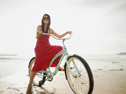 Hispanic woman riding retro bicycle on beach