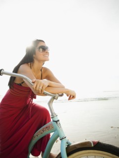 Hispanic woman riding retro bicycle on beach