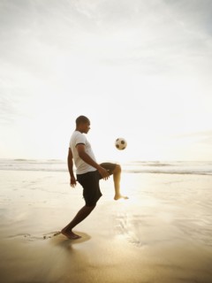 Black man playing with soccer ball on beach