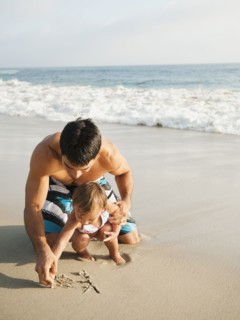 Mixed race father and daughter writing in sand together