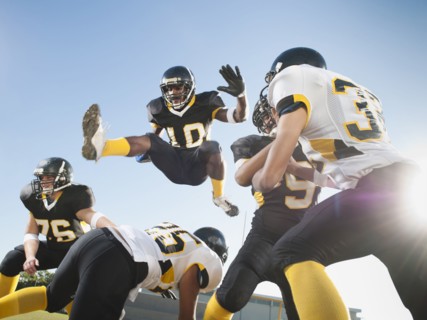Football player leaping over players on football field