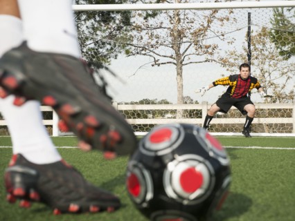 Soccer player kicking ball into goal on soccer field