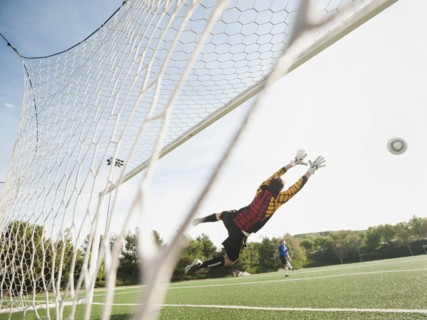 Mixed race goalkeeper in mid-air protecting goal