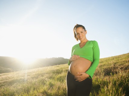 Pregnant Hispanic woman caressing stomach in field
