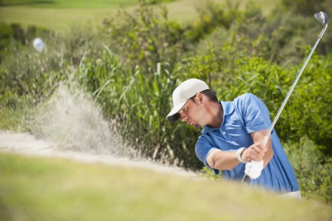 Caucasian golfer hitting ball out of bunker