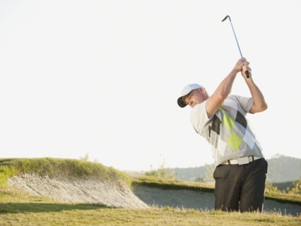 Caucasian golfer hitting ball out of bunker